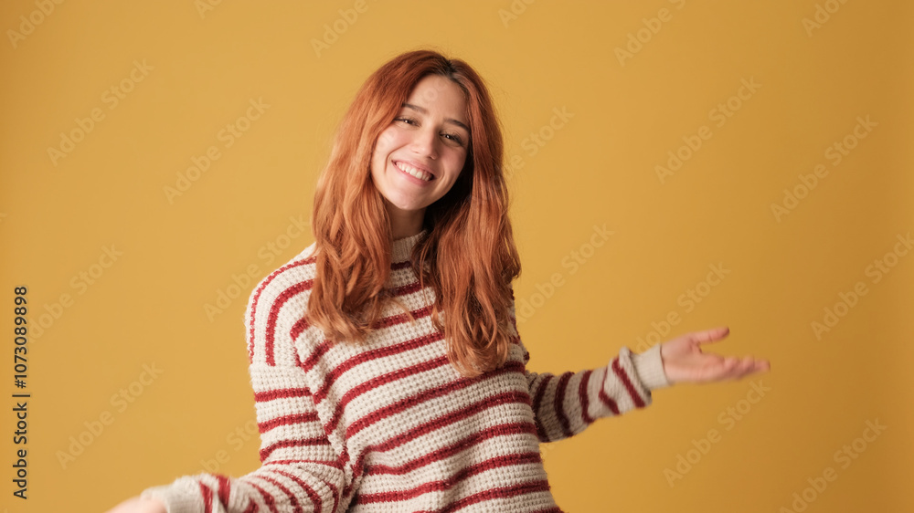 Happy red-haired woman dressed in sweater is having fun dancing on yellow background. Beautiful girl poses in studio with blank space on yellow wall for your promotion Happy red-haired woman dressed in sweater is having fun dancing on yellow background. Beautiful girl poses in studio with blank space on yellow wall for your promotion