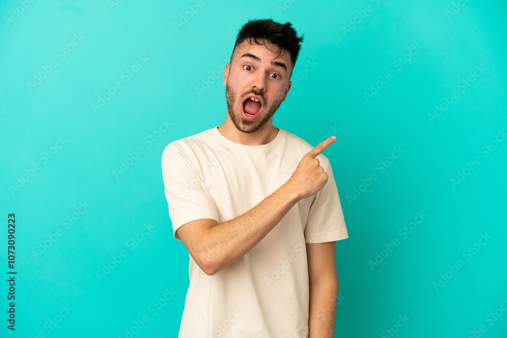 Young caucasian man isolated on blue background surprised and pointing side Young caucasian man isolated on blue background surprised and pointing side