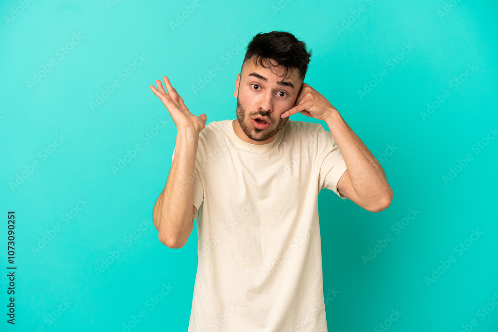 Young caucasian man isolated on blue background making phone gesture and doubting Young caucasian man isolated on blue background making phone gesture and doubting
