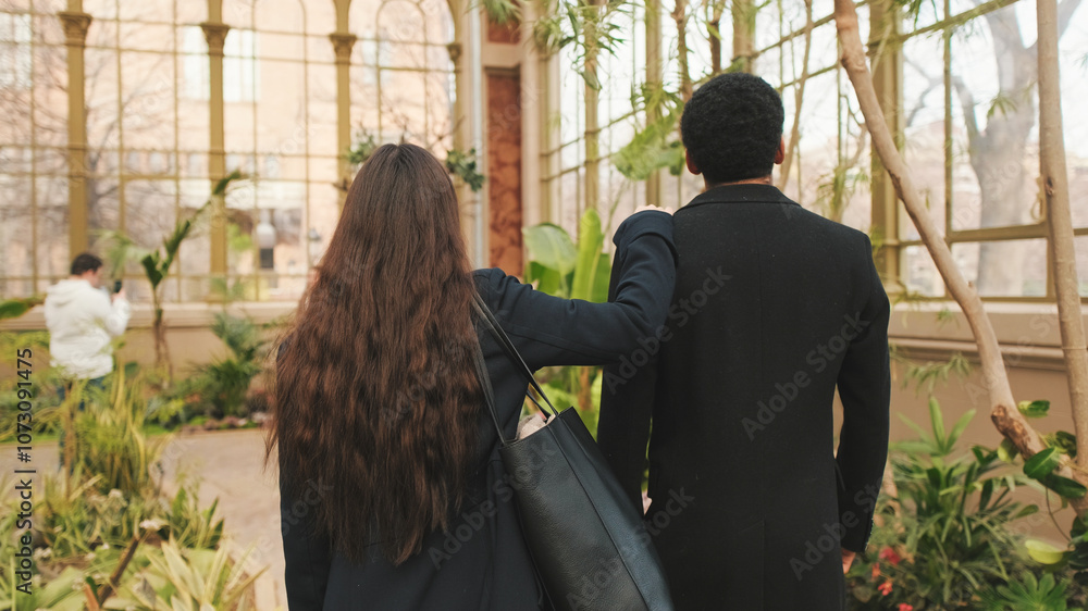 Rear view of couple enjoying leisurely walk in greenhouse, surrounded by lush plants Rear view of couple enjoying leisurely walk in greenhouse, surrounded by lush plants
