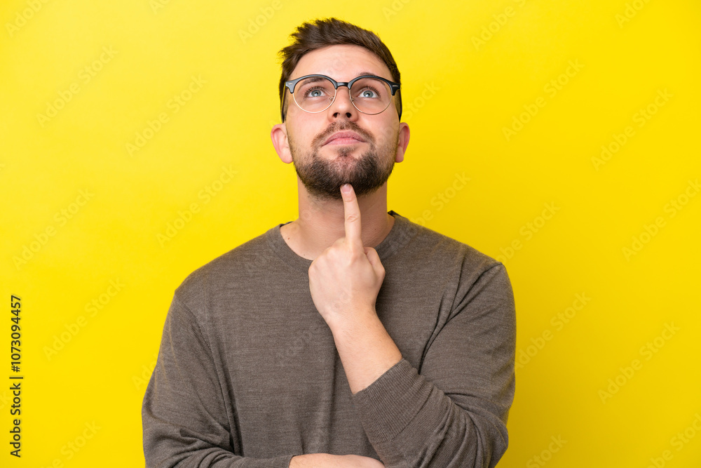 Young caucasian man isolated on yellow background With glasses and looking up Young caucasian man isolated on yellow background With glasses and looking up