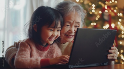 An asian grandmother and her granddaughter are enjoying a video call with family members on a laptop during Christmas. They’re smiling warmly, festive holiday moments by cozy holiday decorations photo