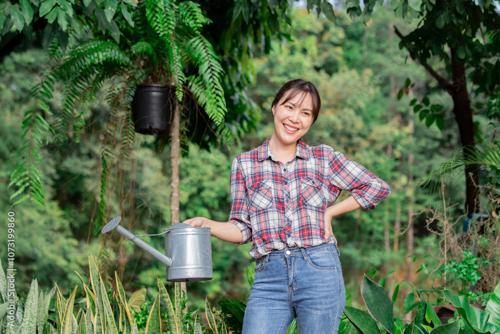 Asian woman in garden, holding watering can, smiling with plaid shirt, jeans. Relaxed, happy. female free time weekend activity. Greenery background, plants around, gardening, tree shop small business Asian woman in garden, holding watering can, smiling with plaid shirt, jeans. Relaxed, happy. female free time weekend activity. Greenery background, plants around, gardening, tree shop small business