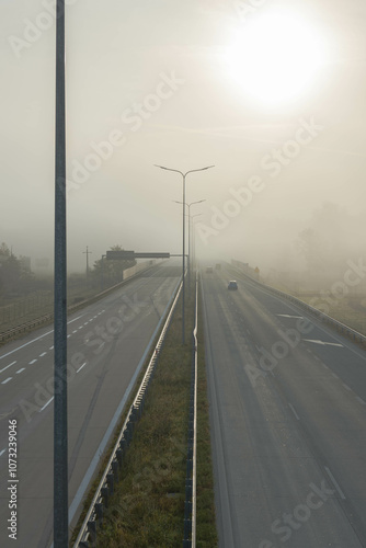 Obraz na płótnie Dwujezdniowa, czteropasmowa autostrada. Nad jezdnią unosi się mgła ograniczająca widoczność. Jest ona od przodu oświetlana promieniami słońca. w salonie