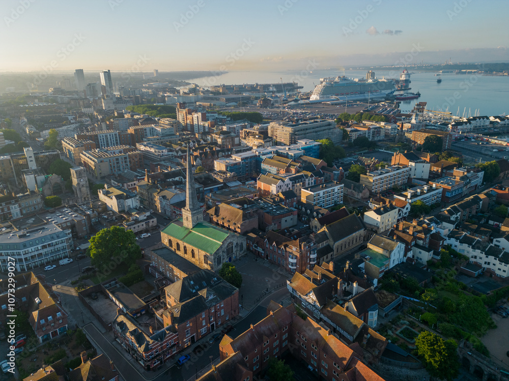 Panorama of Southampton old town with church and a cruise ship at beautiful sunrise. Aerial view of the seaside city. Large cruise ship moored at the terminal near marina. Air pollution and hazy sky.
