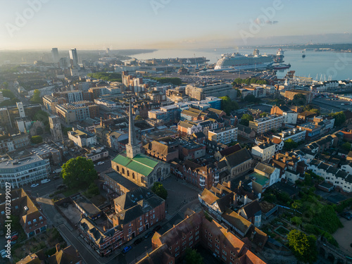 Obraz na płótnie Panorama of Southampton old town with church and a cruise ship at beautiful sunrise. Aerial view of the seaside city. Large cruise ship moored at the terminal near marina. Air pollution and hazy sky. w salonie