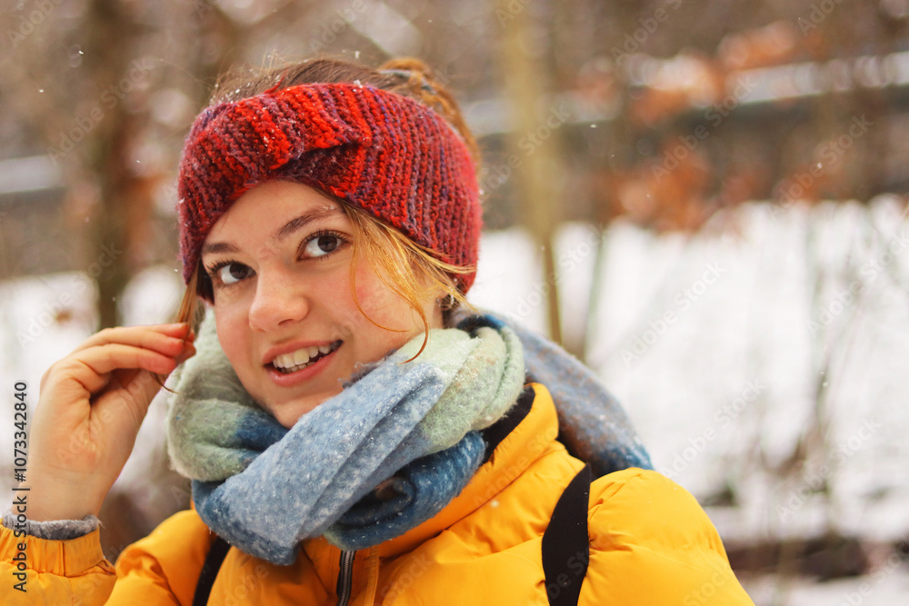 Closeup portrait of a smiling young woman wearing a red knit headband, scarf, and yellow jacket on a cold winter day. Girl dressed warmly surrounded by a blurred snowy background.
Closeup portrait of a smiling young woman wearing a red knit headband, scarf, and yellow jacket on a cold winter day. Girl dressed warmly surrounded by a blurred snowy background.