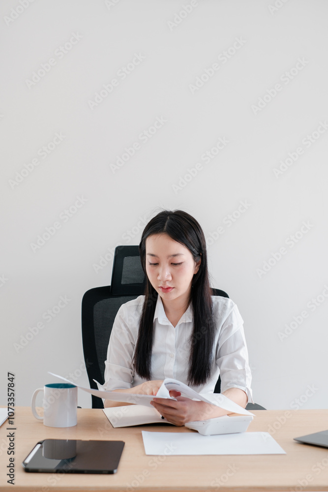 Focused businesswoman reviewing paperwork at a contemporary office desk, surrounded by modern gadgets and minimalist decor. Focused businesswoman reviewing paperwork at a contemporary office desk, surrounded by modern gadgets and minimalist decor.