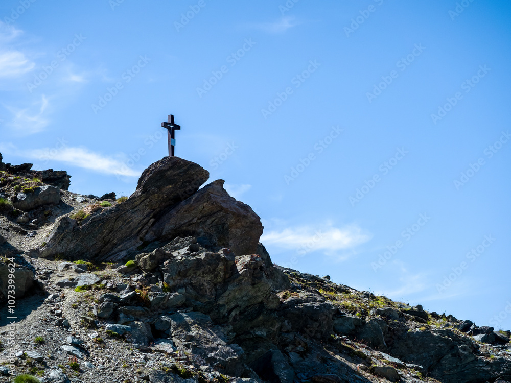 Black cross standing on top of cliff rock formation on blue sky background with copy space. Silhouettes of cross standing on the cliff, at tourist trail view with mountains in Zermatt, Switzerland. Black cross standing on top of cliff rock formation on blue sky background with copy space. Silhouettes of cross standing on the cliff, at tourist trail view with mountains in Zermatt, Switzerland.