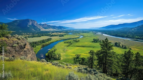 A panoramic view of a river winding through a green valley, surrounded by mountains on either side. The sky is blue and clear, with a few clouds.