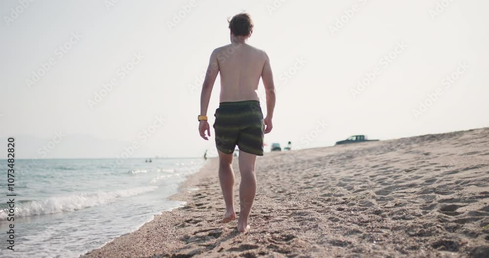 Young man walking on a sandy beach at sunset, peaceful seaside stroll