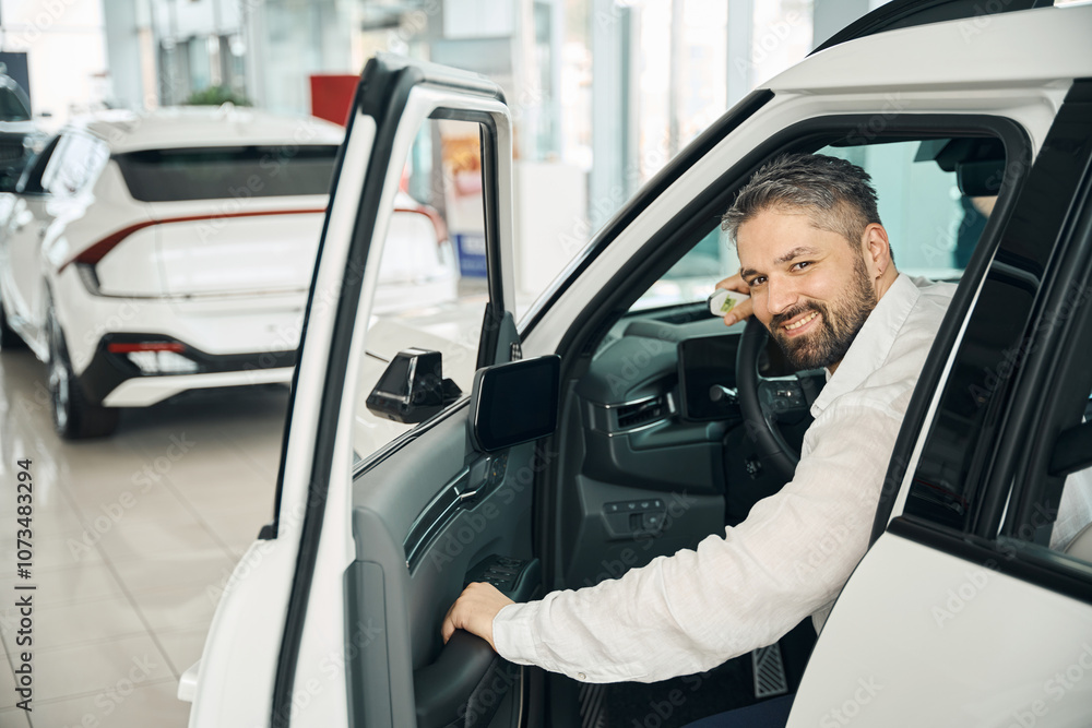 Happy man sitting in the new car with key in auto salon