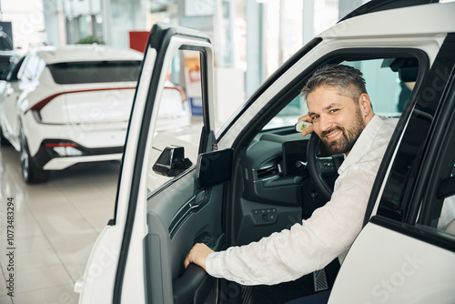 Obraz na płótnie Happy man sitting in the new car with key in auto salon w salonie