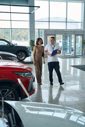 Obraz na płótnie Salesman manager with file folder and female customer standing in car showroom w salonie