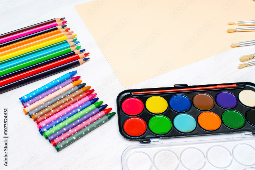 Naklejka premium Watercolor oil paints,paintbrushes,colorful pencils,pastel crayons,blank watercolor paper pad.Creativity creation.Artist's stuff.Flatlay of drawing supplies