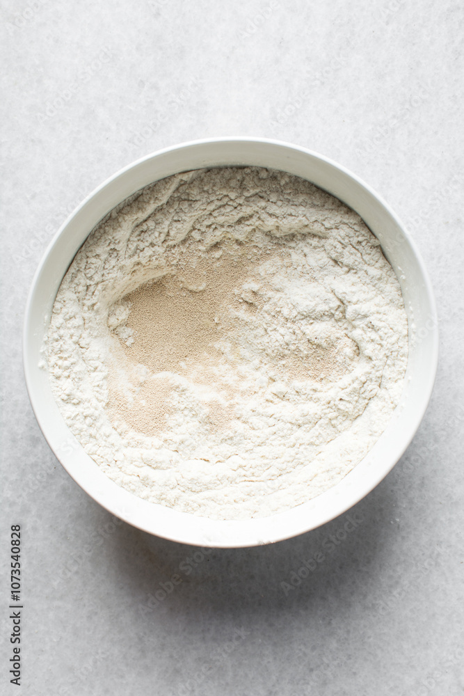Overhead view of ingredients for making puff-puff in a white ceramic bowl, yeast flour sugar in a mixing bowl, process of making puff-puff Overhead view of ingredients for making puff-puff in a white ceramic bowl, yeast flour sugar in a mixing bowl, process of making puff-puff