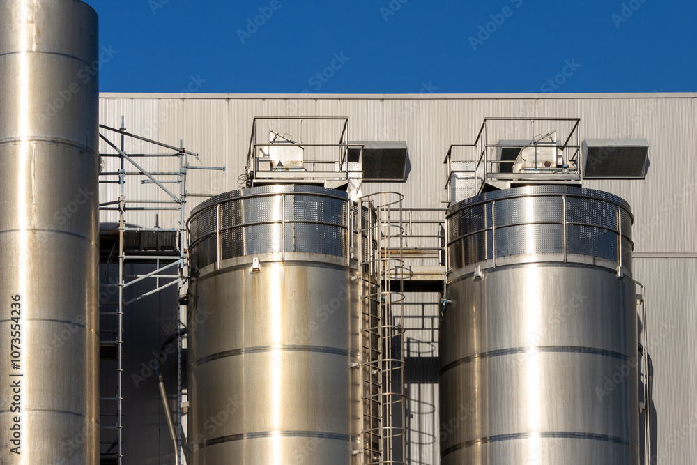 Industrial silos gleaming under a clear blue sky at a modern processing plant Industrial silos gleaming under a clear blue sky at a modern processing plant