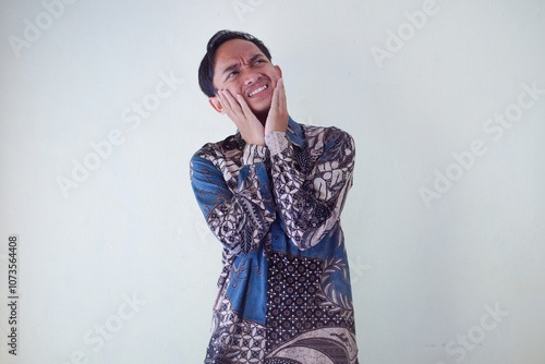 Handsome Asian young man wearing batik shirt showing gesture of thinking about something, memorizing on white background photo