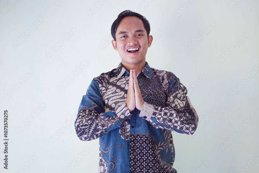 Smiling Asian man wearing batik shirt, showing hand gesture of apology and welcome. Advertising concept. Smiling Asian man wearing batik shirt, showing hand gesture of apology and welcome. Advertising concept.