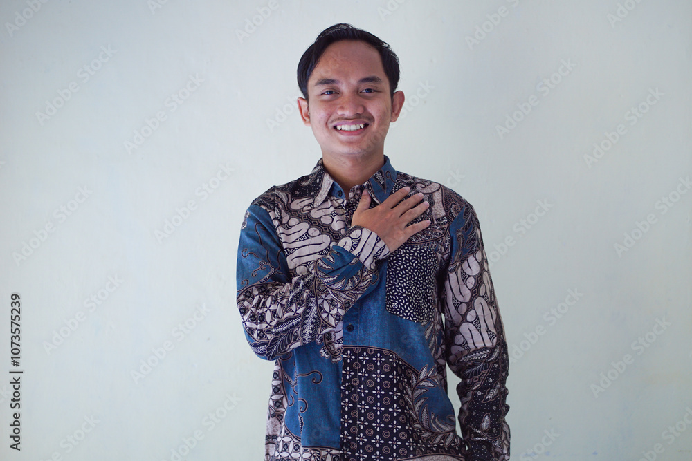 Smiling Asian man wearing batik shirt, showing hand gesture of apology and welcome. Advertising concept.