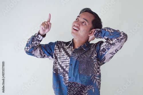 Handsome Asian young man wearing batik shirt showing gesture of thinking about something, memorizing on white background photo