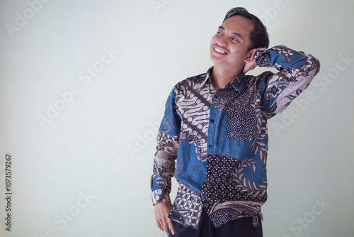 Handsome Asian young man wearing batik shirt showing gesture of thinking about something, memorizing on white background photo