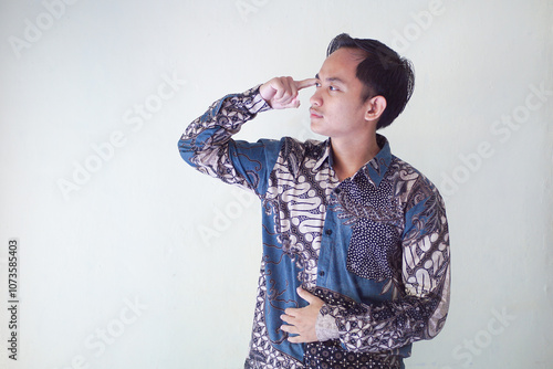 Handsome Asian young man wearing batik shirt showing gesture of thinking about something, memorizing on white background photo