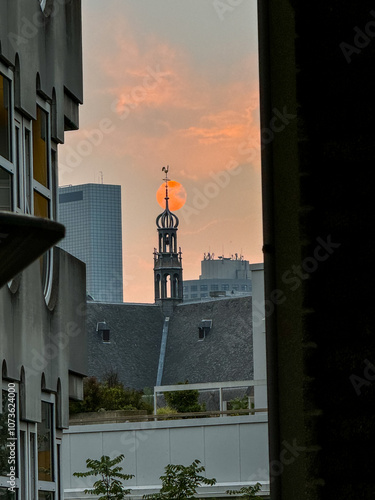 Rotterdam, Netherlands - August 2, 2024: Sunset with a church spire in the foreground seen in Rotterdam in the Netherlands
 photo