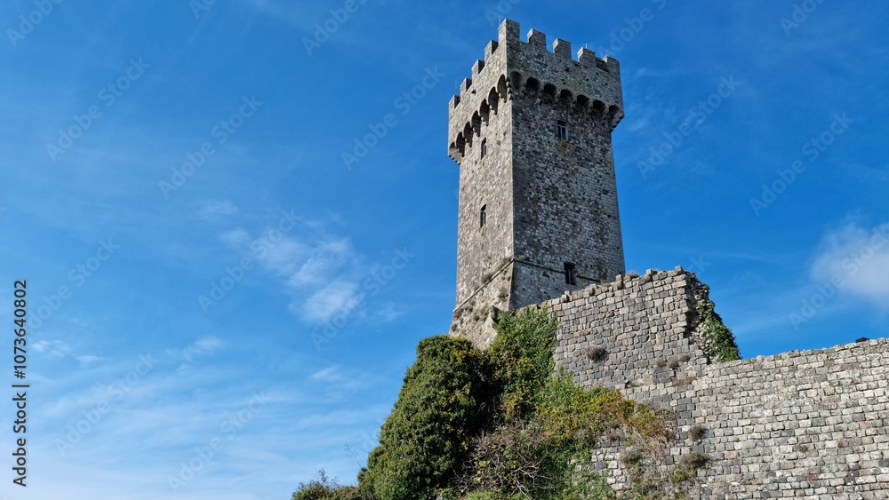 Historic stone tower with battlements under a clear blue sky, surrounded by foliage. Historic stone tower with battlements under a clear blue sky, surrounded by foliage.