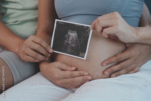 The hands of the pregnant parents hold the seven-month pregnant mother's belly to show the results of the fetal examination in the womb.