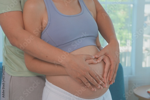 Obraz na płótnie Asian husband and wife stand hugging each other, father holding hands with wife making a heart shape on the womb, wife is 7 months pregnant and happy with first child. w salonie