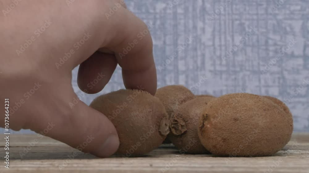 A Hand Reaching Out for Fresh, Juicy Kiwifruits on a Beautiful Wooden Table Surface A Hand Reaching Out for Fresh, Juicy Kiwifruits on a Beautiful Wooden Table Surface