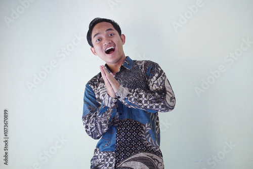 young Asian man wearing a batik shirt with a facial expression of surprise, surprise and amazement