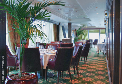 Formal and elegant ocean view dining room restaurant onboard luxury cruiseship or cruise ship liner with set tables in Country Club interior design style and ceiling ambient lighting