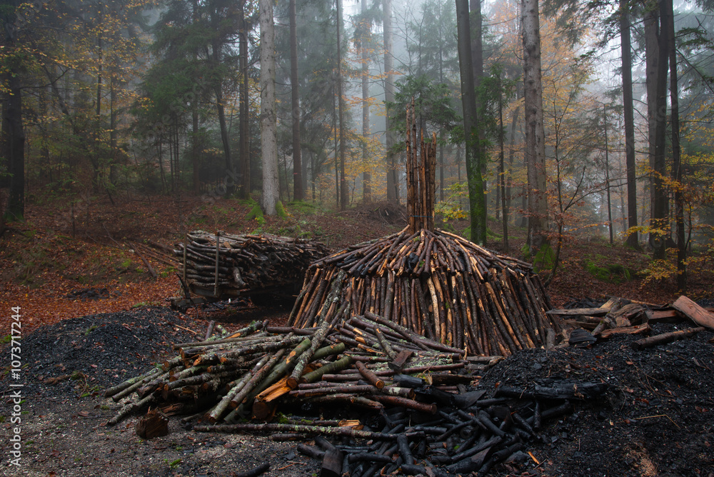 Charcoal pile burning in misty forest setting with stacked firewood Charcoal pile burning in misty forest setting with stacked firewood