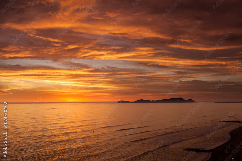 Fototapeta premium As the sun sets over San Lorenzo Island, the view from Miraflores becomes pure magic .The island silhouettes against a sky ablaze with color, while the ocean whispers of infinite horizons. 