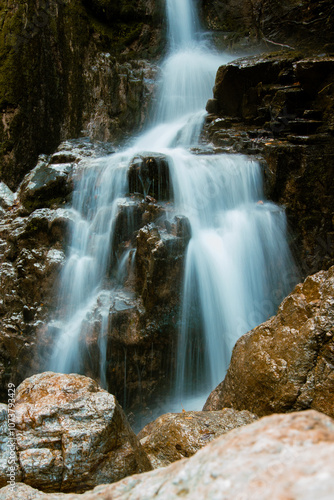 Serene waterfall cascades down moss-covered rocks, surrounded by the vibrant colors of autumn foliage.