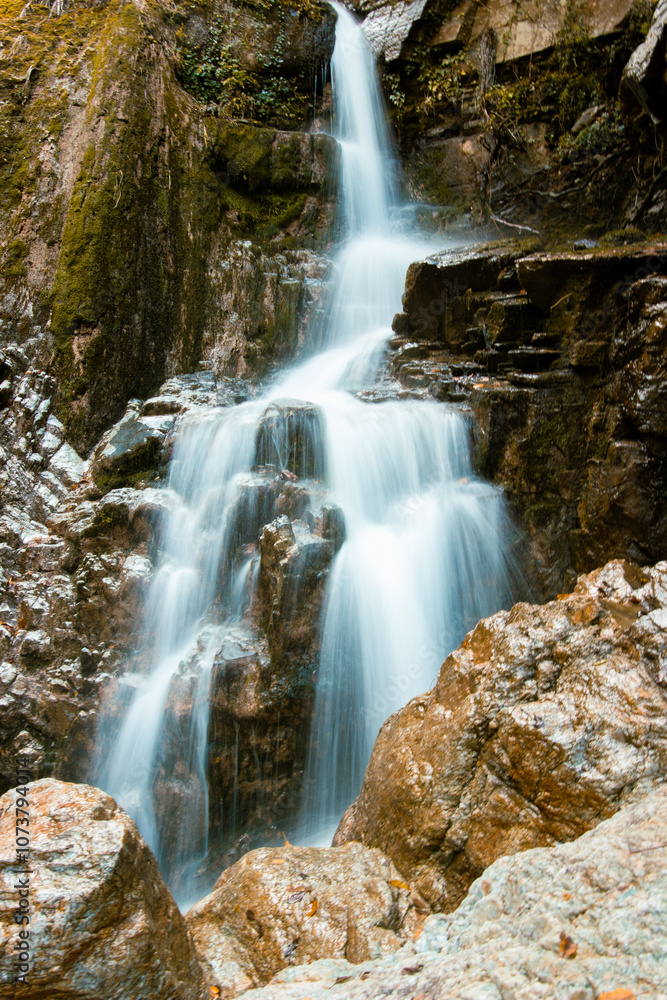 Serene waterfall cascades down moss-covered rocks, surrounded by the vibrant colors of autumn foliage.