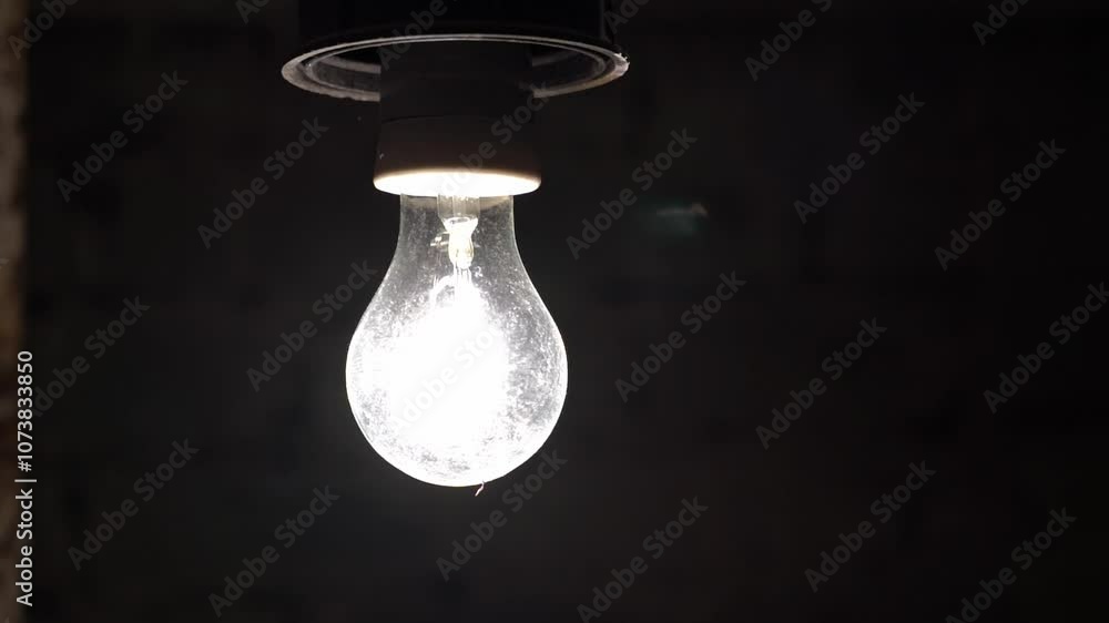 A light bulb in a dark basement blinks due to voltage droA light bulb in a dark basement blinks due to voltage drop. An old glass light bulb filled with a warm yellow glow looks truly charming. 4k is A light bulb in a dark basement blinks due to voltage droA light bulb in a dark basement blinks due to voltage drop. An old glass light bulb filled with a warm yellow glow looks truly charming. 4k is