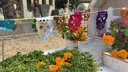 string of papel picado in shape of skulls decorating tomb in graveyard