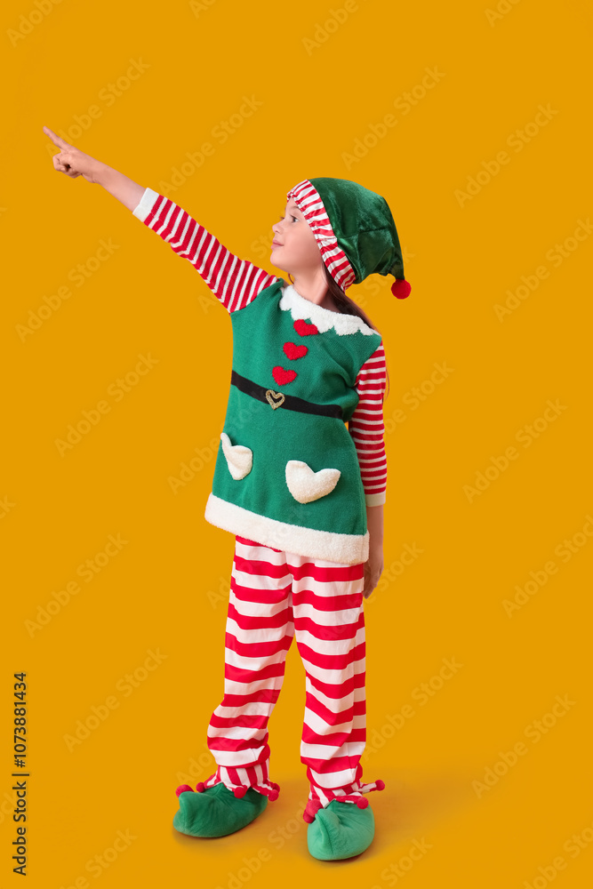 Obraz premium Cute little girl in elf's costume pointing at something on yellow background