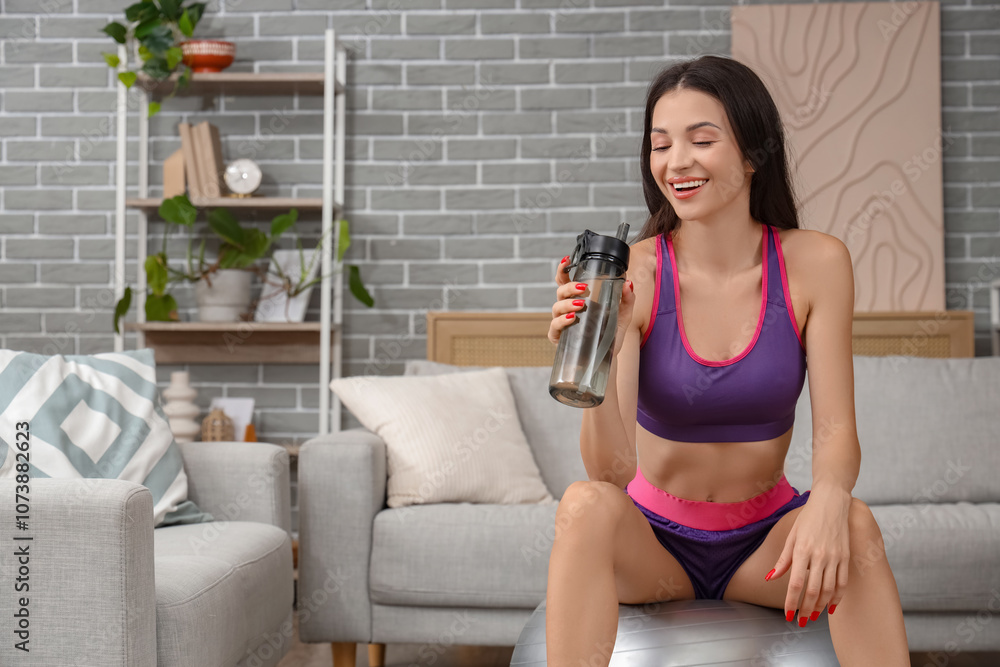 Sporty young woman with water bottle sitting on fitball at home Sporty young woman with water bottle sitting on fitball at home