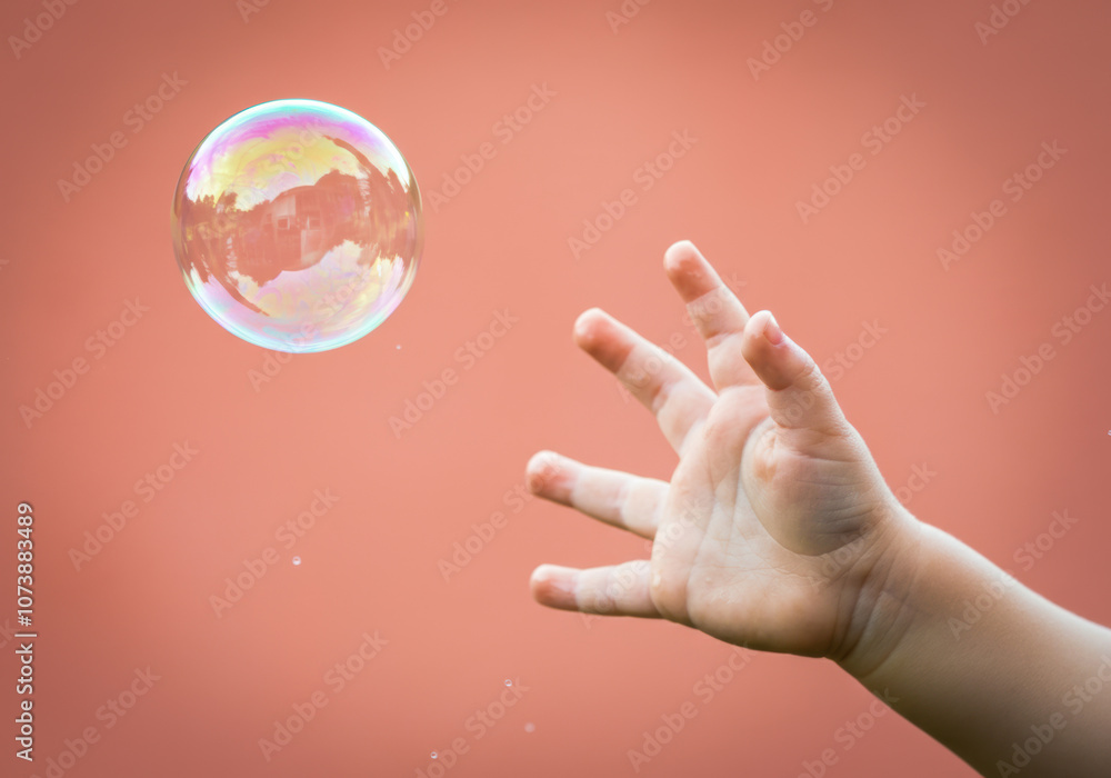 Child reaching for a soap bubble against a warm, textured background on a sunny day Child reaching for a soap bubble against a warm, textured background on a sunny day