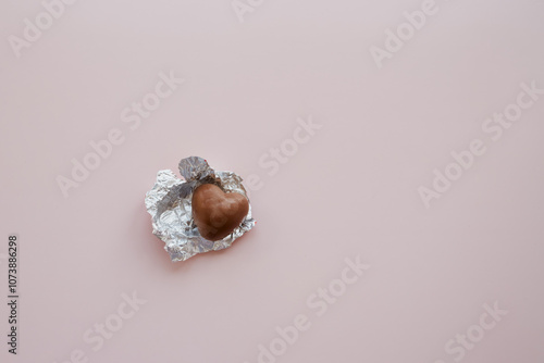 A heart-shaped chocolate candy in a red wrapper unwrapped on a pink background, sweets for Valentine's Day, open heart, confession of love, heart-shaped candies.