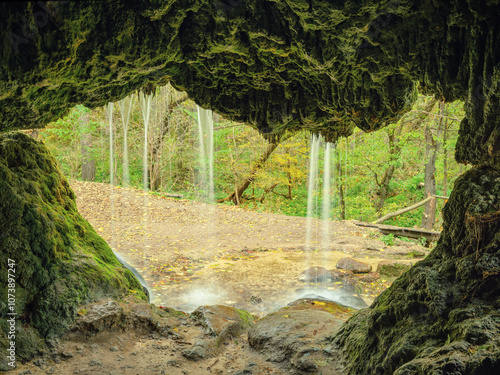 view from natural cave in rock and waterfall flows in forest
