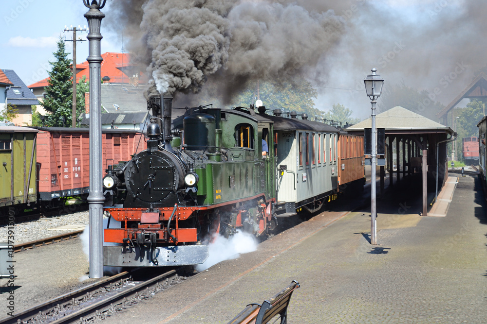 Obraz premium A smoking steam locomotive carrying passengers stands at the station.