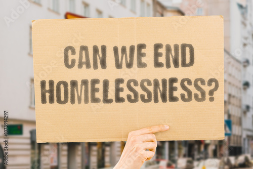 The phrase 'Can We End Homelessness?' on a banner in a person's hand. Human holds a cardboard with an inscription. Compassion. Dignity. Shelter. Support. Community. Change. Hope