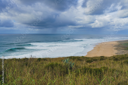 Impending storm casting a dramatic light over the serene and wild Nazare beach.