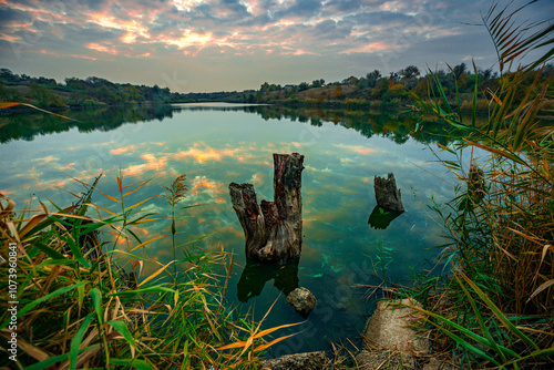 Morning on the river with sunrise and clouds reflections on water,golden sunrise .Old and fallen trees stands on the beach,blue and beautiful water , red and golden sunrise.River at autumn morning.