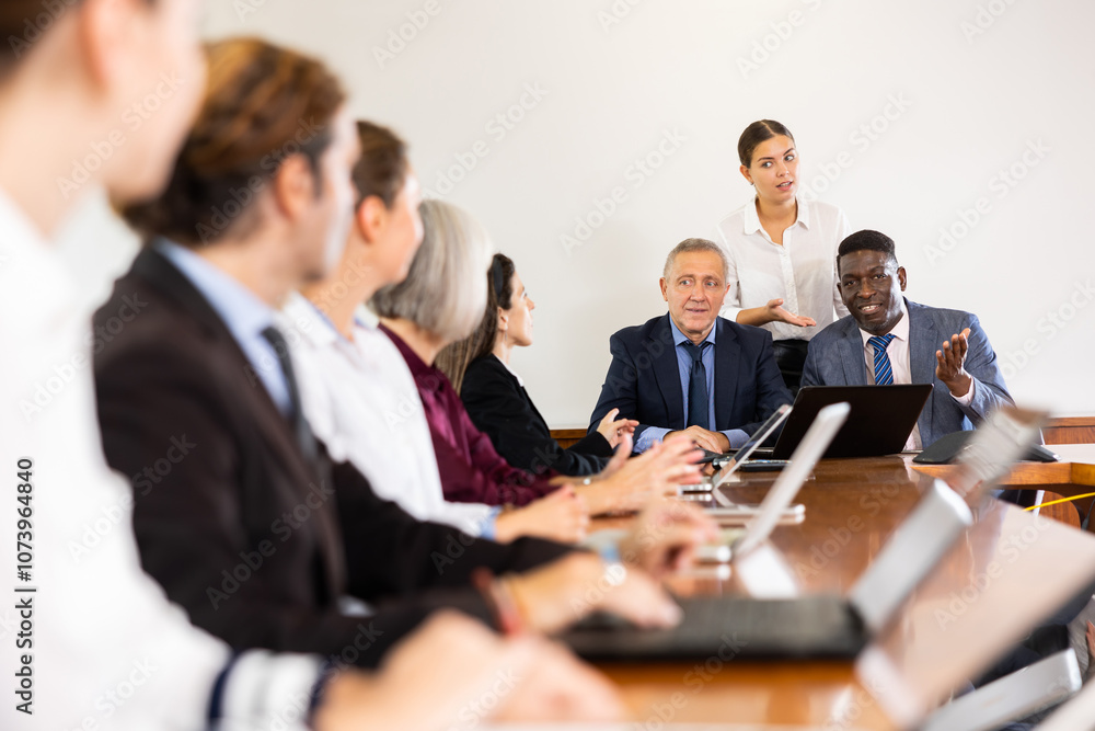 Two mid-aged male executive managers leading staff meeting and having discussion with office employees while a young white female administrative assistant helping them in coordinating the meeting Two mid-aged male executive managers leading staff meeting and having discussion with office employees while a young white female administrative assistant helping them in coordinating the meeting